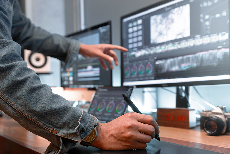 A student uses a tablet and computer screens to learn post-production editing for a digital media degree.