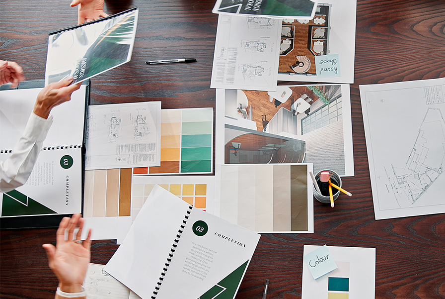 A table covered with interior design course materials, including room design blueprints, color palettes, stationeries, and project binders.