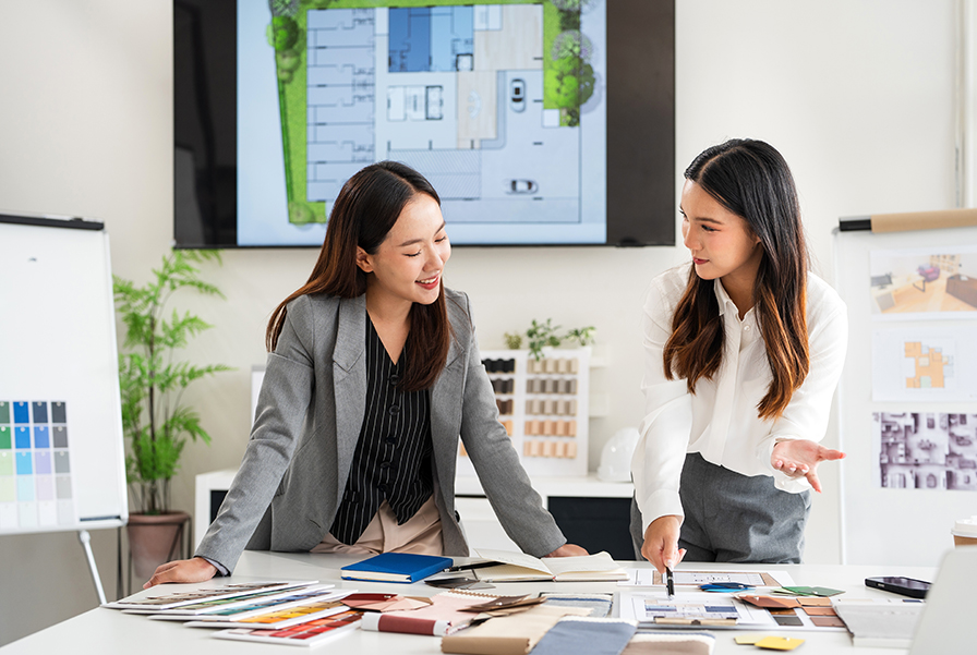 Two interior designers at an interior design company discussing room design blueprints and material choices.
