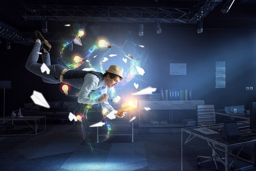 A man in a vest and hat floats in a dark office, holding a glowing book while light bulbs and colored energy swirl around him.