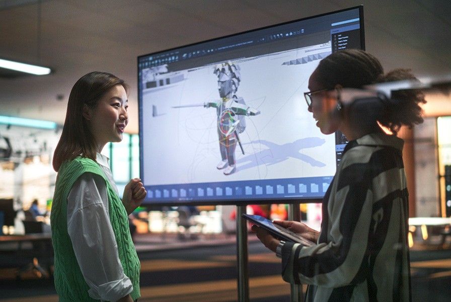 Two game developers standing and talking in front of a screen that shows a character game design.