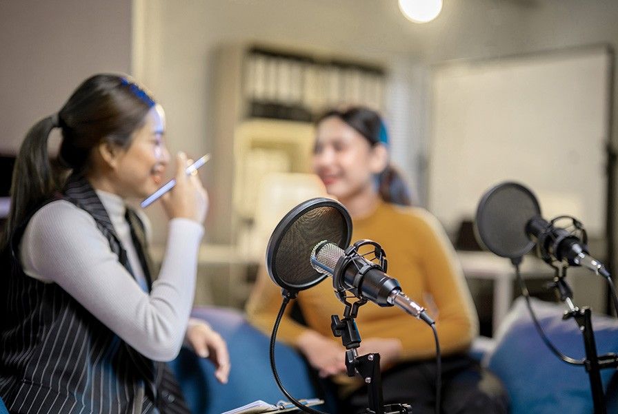 Two women talking in front of two microphones in a recording studio.