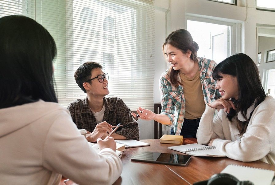 A group of people having a discussion while sitting in a table that has a tablet and notebooks open.