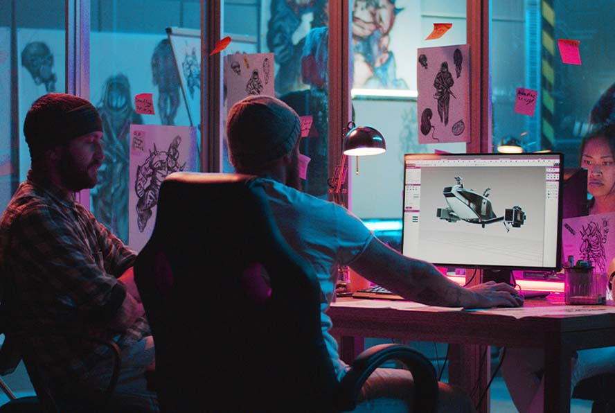 Team collaborating at a desk while reviewing a 3D design on a computer screen in a creative studio.