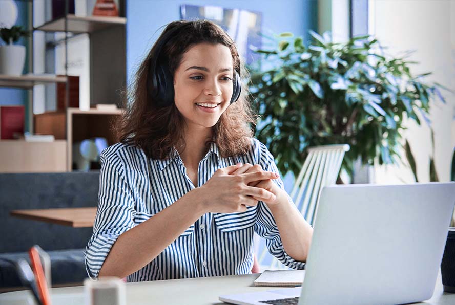 Person wearing headphones smiling while working on a laptop at a desk.